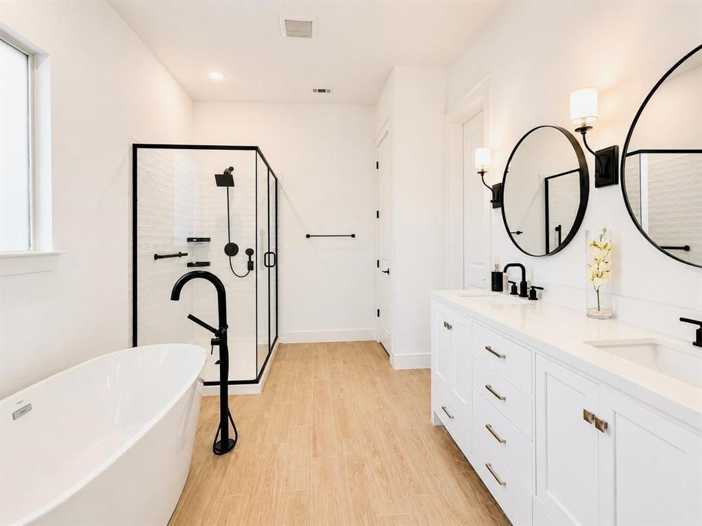 Dual-vanity cabinet with quartz countertop, undermount sinks, and matte black fixtures, paired with a freestanding soaking tub, walk-in glass shower, and wood-finish flooring