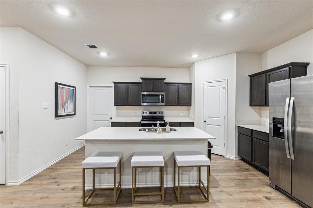 Kitchen featuring dark cabinetry, a central island with a solid-surface countertop, stainless steel appliances, and wood-finish flooring