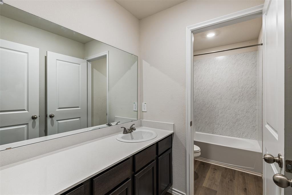 Bathroom vanity featuring dark-toned cabinetry, a light-colored solid surface countertop, an integrated sink with a dual-handle faucet, and a wall-to-wall mirror