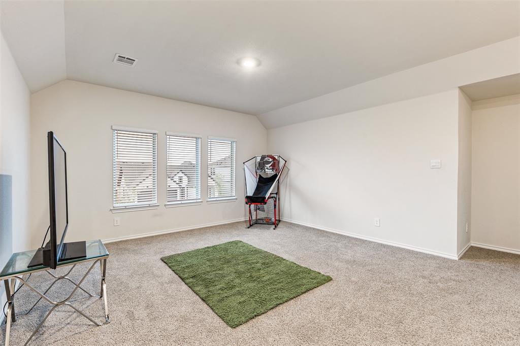 Neutral-toned interior space featuring vaulted ceilings, plush carpeting, and a trio of windows with horizontal blinds