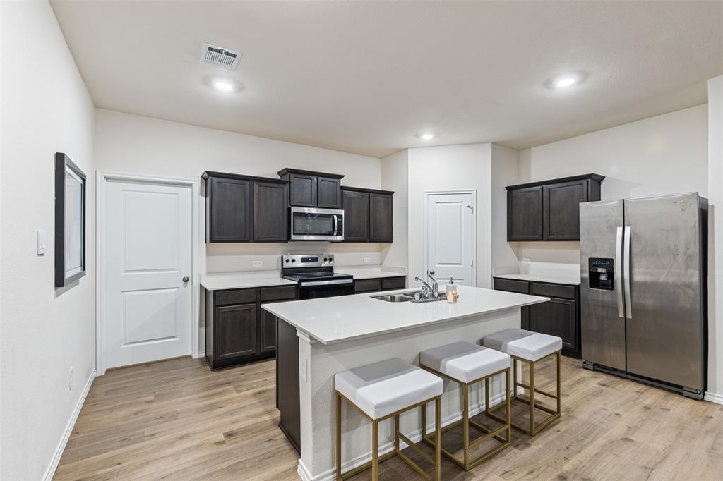 Kitchen featuring dark cabinetry, quartz countertops, a central island with an integrated stainless steel sink, stainless steel appliances, and wood-finish flooring
