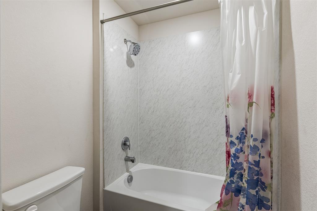 Full-size bathtub with light-toned wall surround, shower head, chrome-finish plumbing fixtures, and a dual-flush toilet