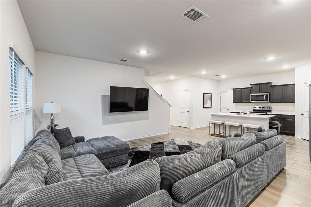 Open-concept interior featuring wood-finish flooring, recessed lighting, and a kitchen equipped with dark cabinetry and a central island with a stone-finish countertop