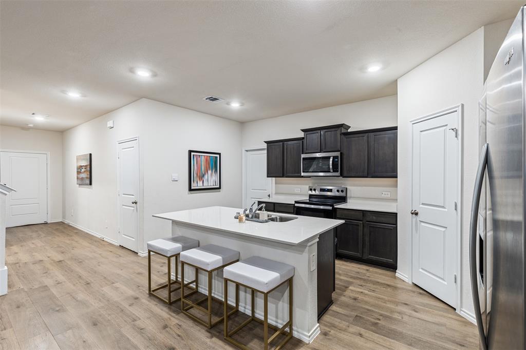 Kitchen featuring wood-finish flooring, a central island with a solid-surface countertop, dark-toned cabinetry, recessed lighting, and stainless steel appliances