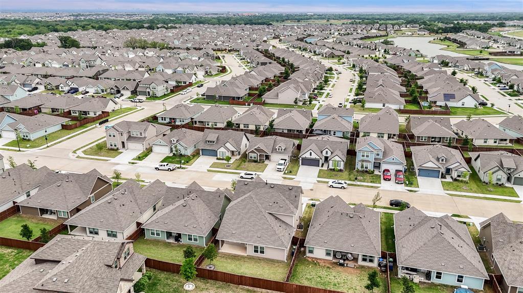 Aerial perspective of a master-planned community featuring residential lots with fenced backyards, paved streets, and a retention pond