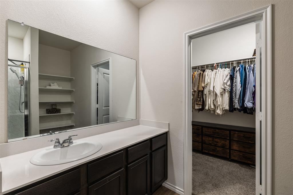 Bathroom featuring a dark-finish wood vanity with a solid-surface countertop, integrated oval basin, large wall-mounted mirror, and a walk-in closet equipped with built-in shelving and drawer storage