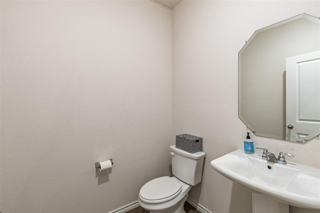 Wall-mounted octagonal mirror, pedestal sink with chrome dual-handle faucet, and ceramic toilet