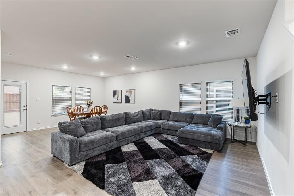 Open-concept interior featuring wood-finish flooring, recessed lighting, and multiple windows with horizontal blinds