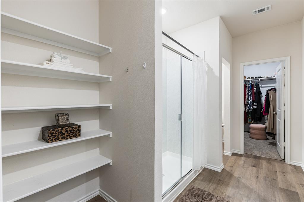 Built-in white shelving, shower enclosure with glass doors, and wood-finish flooring