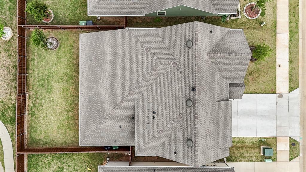 Aerial perspective featuring a multi-pitch asphalt shingle roof, a concrete driveway, and a fenced yard with mature landscaping