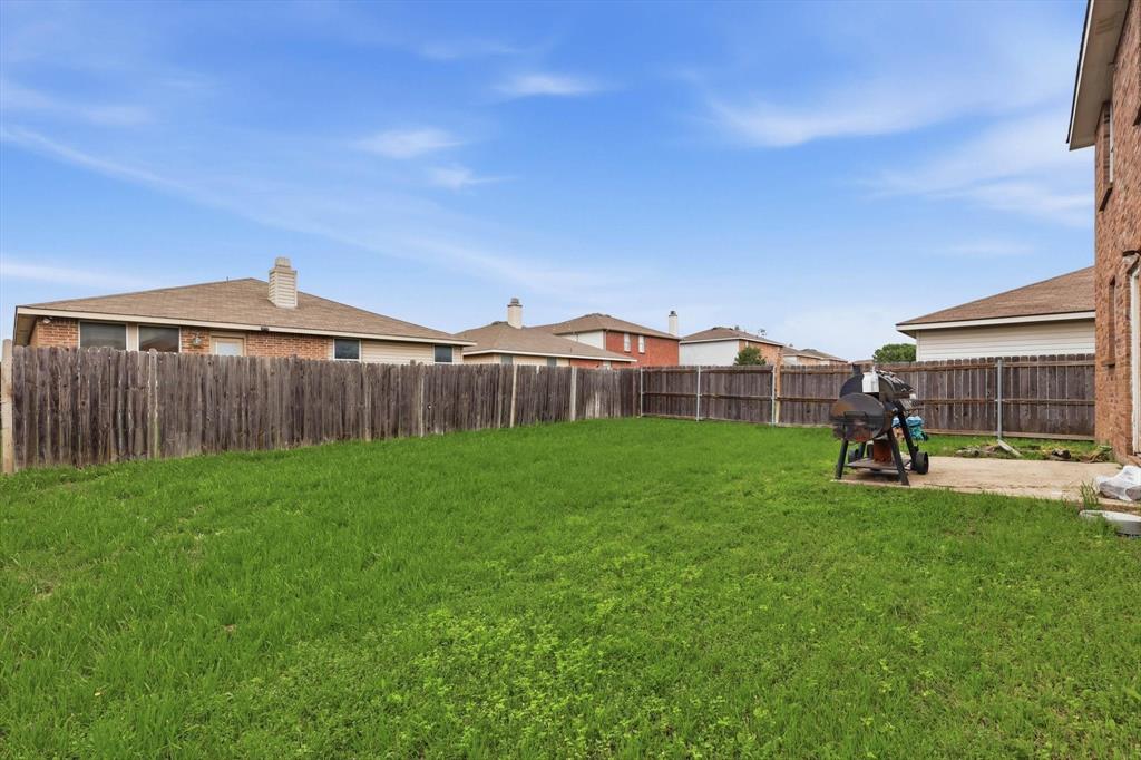 Rear yard featuring an open grass lawn, concrete patio, and a perimeter wood privacy fence
