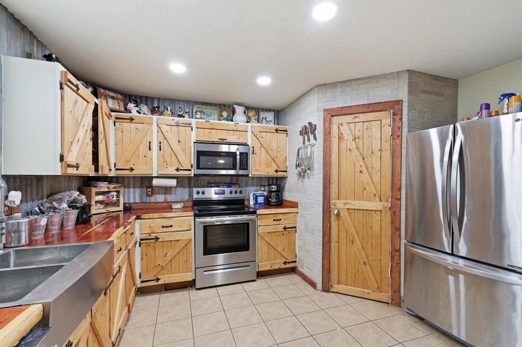 Kitchen featuring custom wood cabinetry with barn-door detailing, stainless steel appliances, corrugated metal backsplash, tiled flooring, and a metal apron-front sink