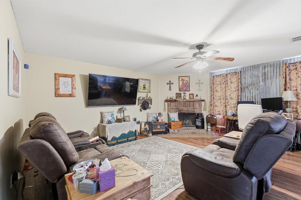 Brick fireplace with wooden mantel, wood-finish flooring, and ceiling fan with light fixture