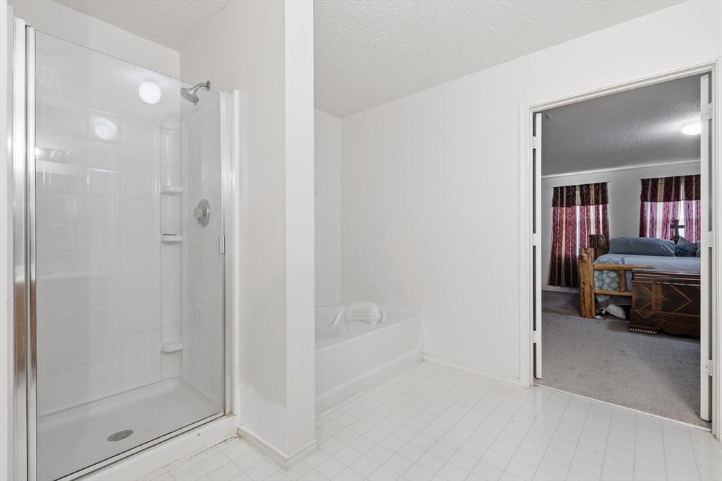 Bathroom featuring a glass-enclosed shower, a deep soaking tub, and tile flooring