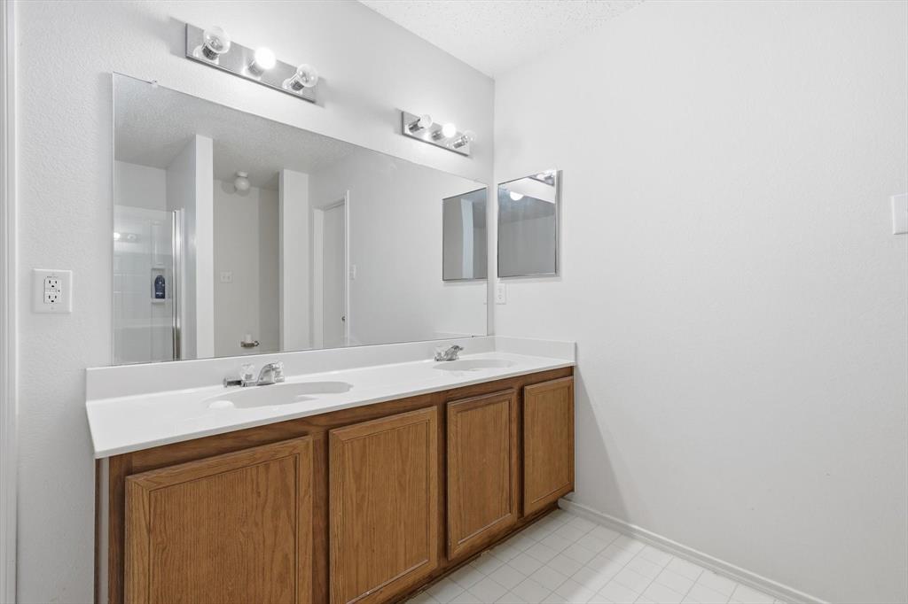 Double vanity featuring wood-finish cabinetry, a solid-surface countertop with integrated dual sinks, a large wall-mounted mirror, and multi-bulb polished chrome light fixtures