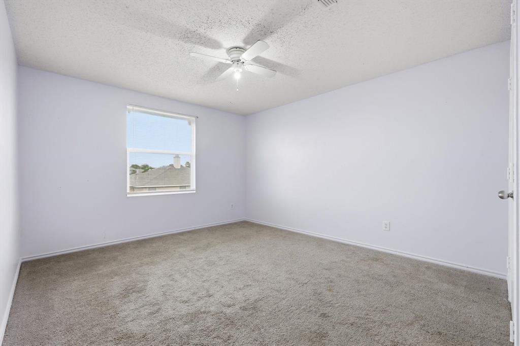 Neutral-toned interior space featuring wall-to-wall carpeting, a single window, and a white ceiling fan with integrated lighting