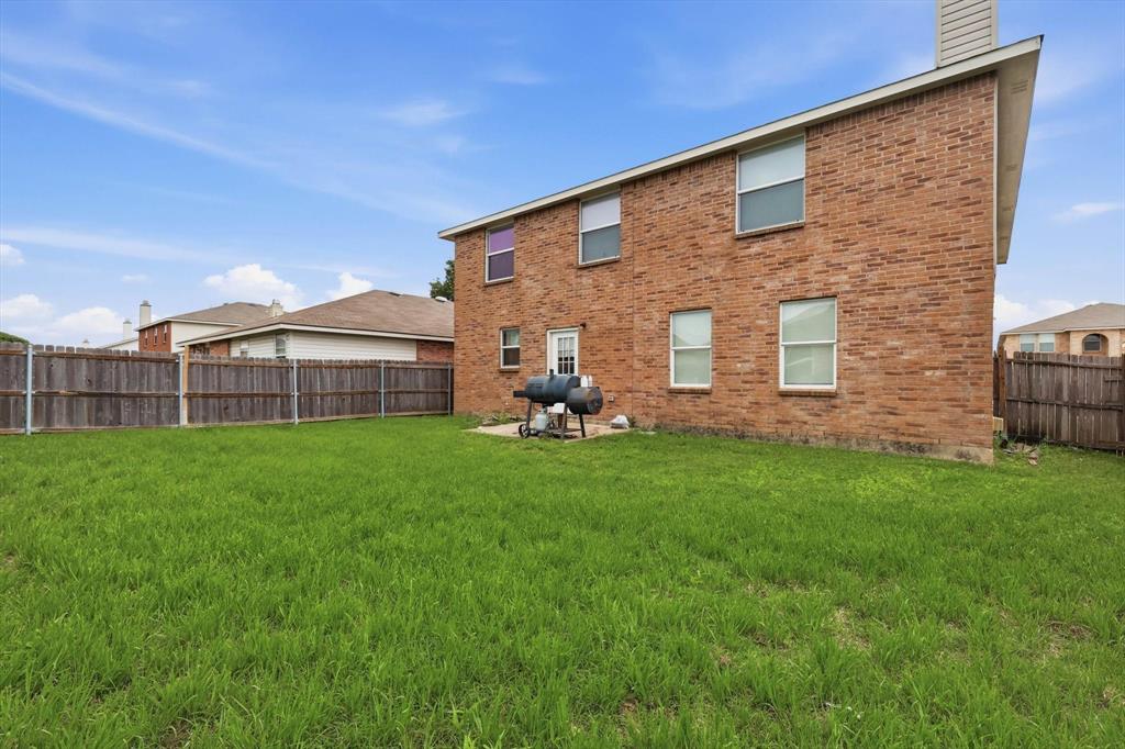 Exterior brick facade featuring a grass lawn, privacy fencing, and a concrete patio