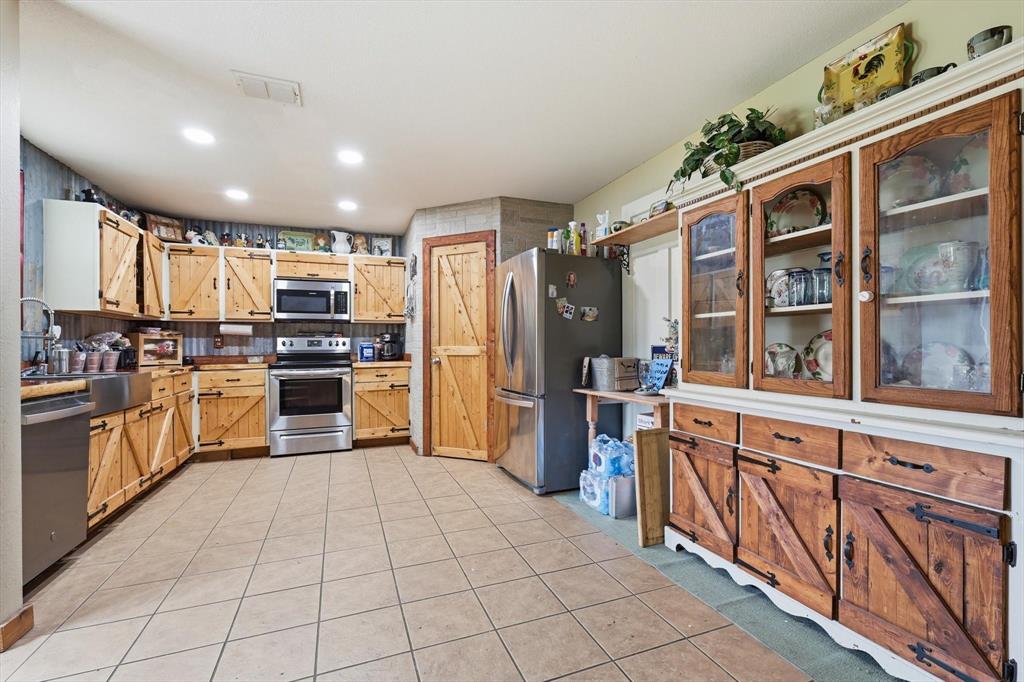 Kitchen featuring custom wood cabinetry with sliding barn-style door detailing, stainless steel appliances, farmhouse sink, recessed lighting, and tile flooring