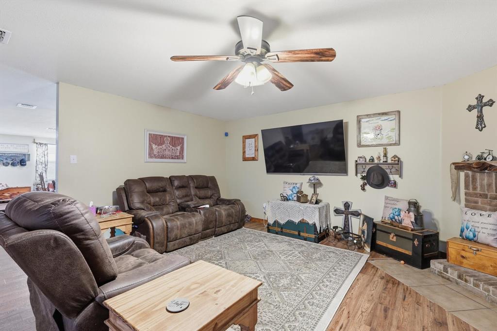 Living area featuring wood-finish flooring, a ceiling fan with integrated lighting, and a brick fireplace hearth