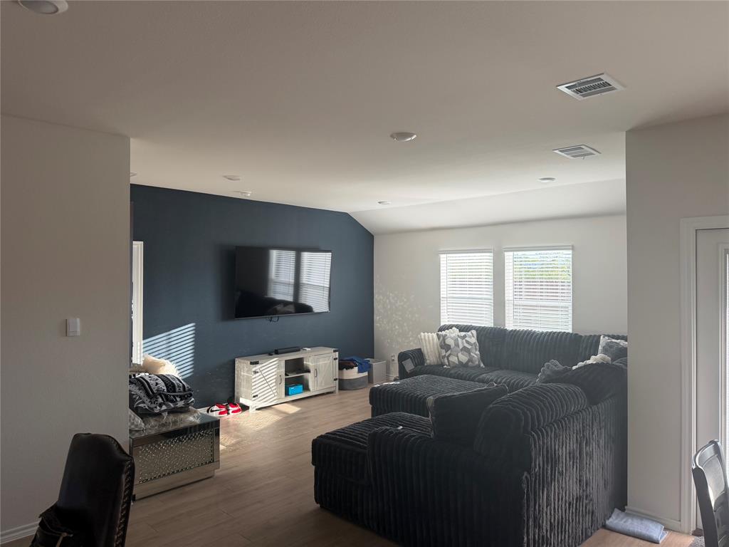 Living area featuring wood-finish flooring, recessed lighting, and a prominent dark accent wall Living area featuring wood-finish flooring, recessed lighting, and a prominent dark accent wall