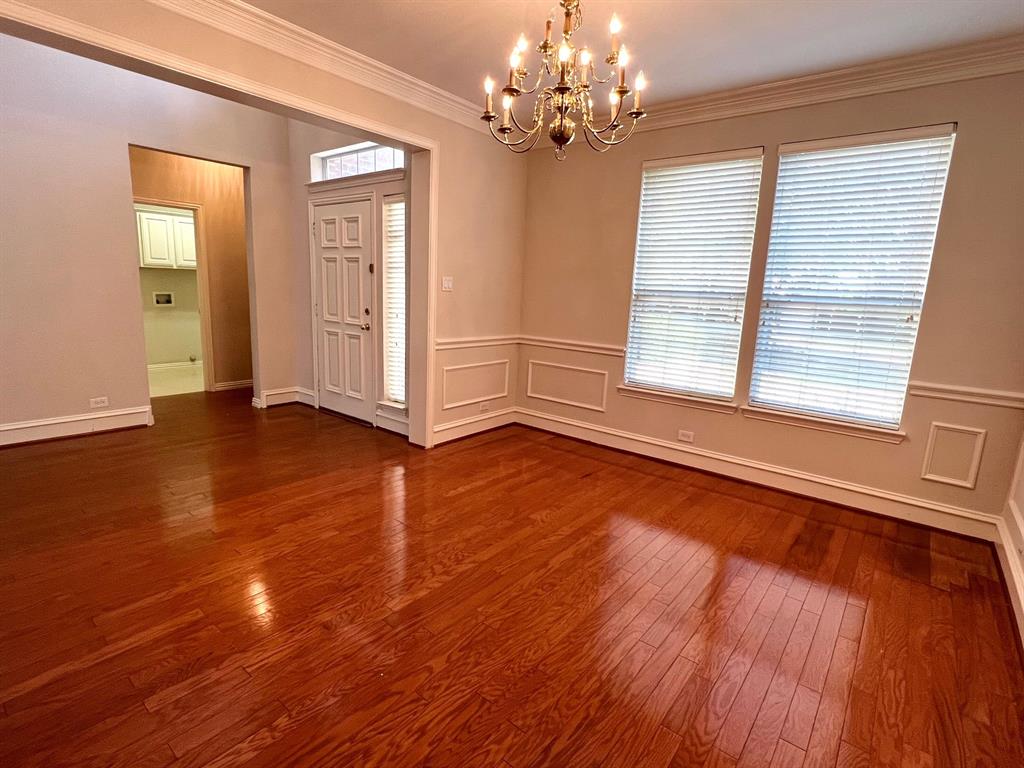 Wood-finish flooring, multi-paneled front door with sidelight, crown molding, chair rail wainscoting, and multi-arm chandelier