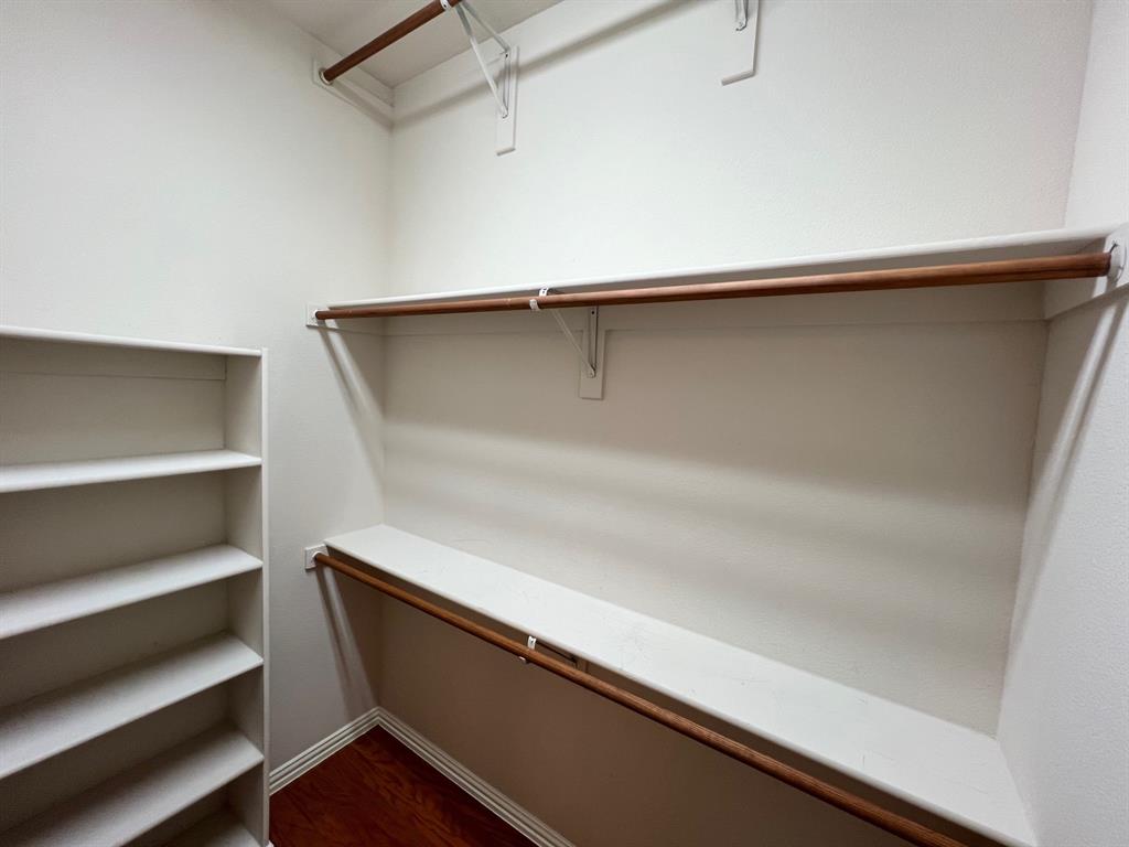 Walk-in closet featuring wood-finish flooring, built-in shelving unit, and multiple tiers of shelving with integrated rods