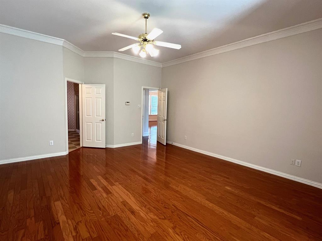 Room interior featuring wood-finish flooring, vaulted ceilings with crown molding, and a central ceiling fan with multi-light fixture