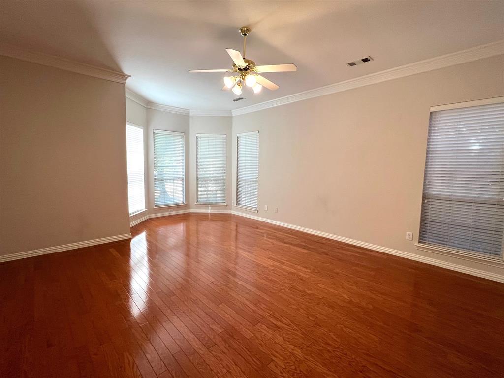 Spacious room featuring wood-finish flooring, crown molding, a bay window configuration, and a central ceiling fan with integrated lighting