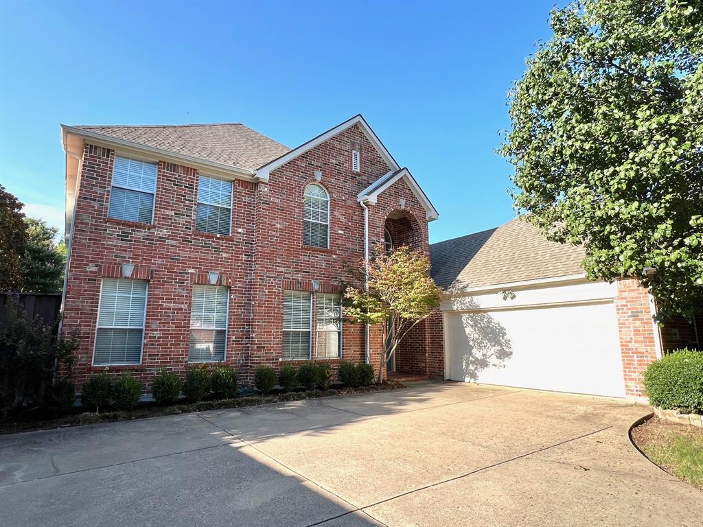 Two-story red brick exterior featuring an arched entryway, shingle roof, multi-pane windows, and an attached two-car garage Two-story red brick exterior featuring an arched entryway, shingle roof, multi-pane windows, and an attached two-car garage