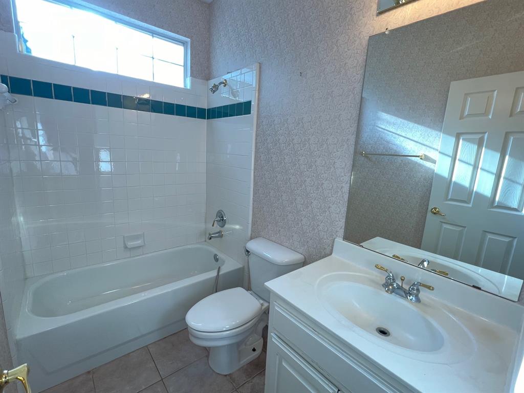 Bathroom featuring a porcelain tub and shower combination with tile surround, vanity with integrated sink, large wall-mounted mirror, and transom window