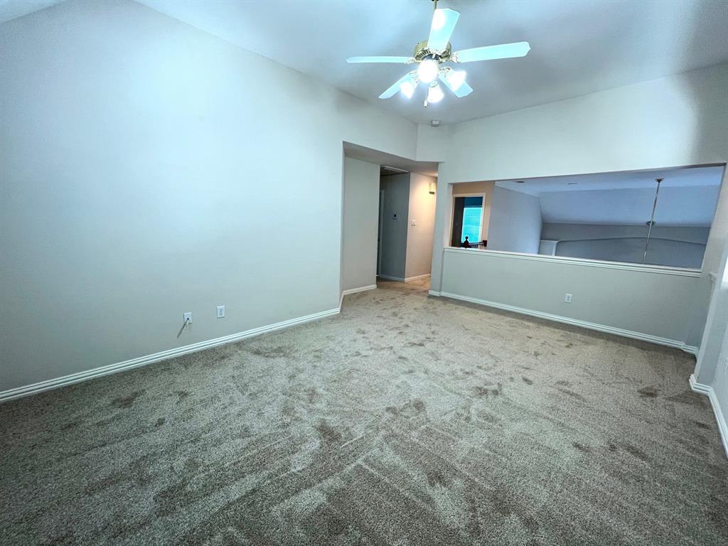 Vaulted ceiling featuring a central ceiling fan with integrated lighting, neutral wall tones, wall-to-wall carpeting, and an open interior partition