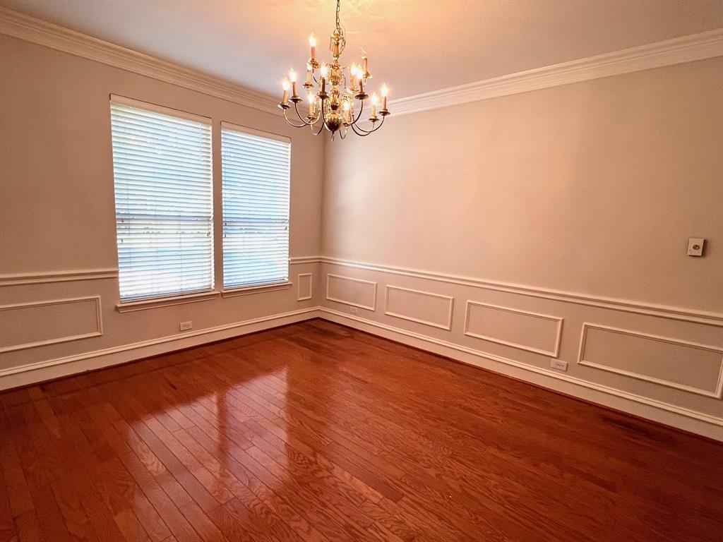 Room featuring wood-finish flooring, wainscoting, crown molding, and a multi-tiered metal chandelier