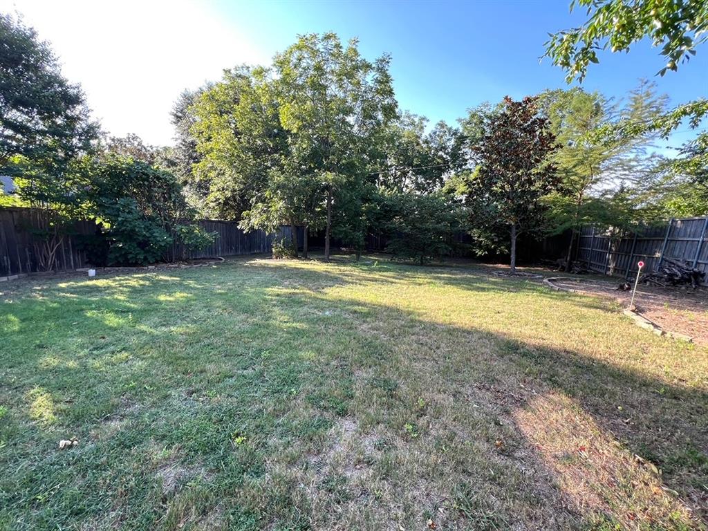Backyard featuring a grass lawn, mature trees, wood privacy fencing, and stone-bordered landscaping beds