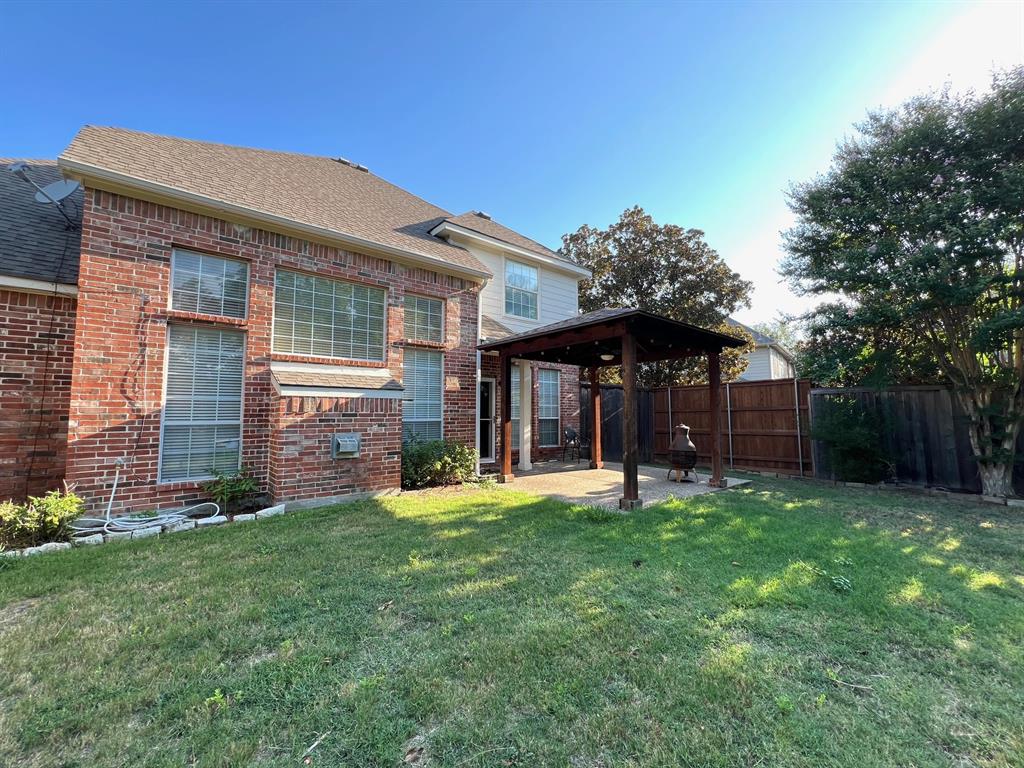 Brick exterior residence featuring a covered wooden pergola, paved patio area, and fenced backyard with mature trees