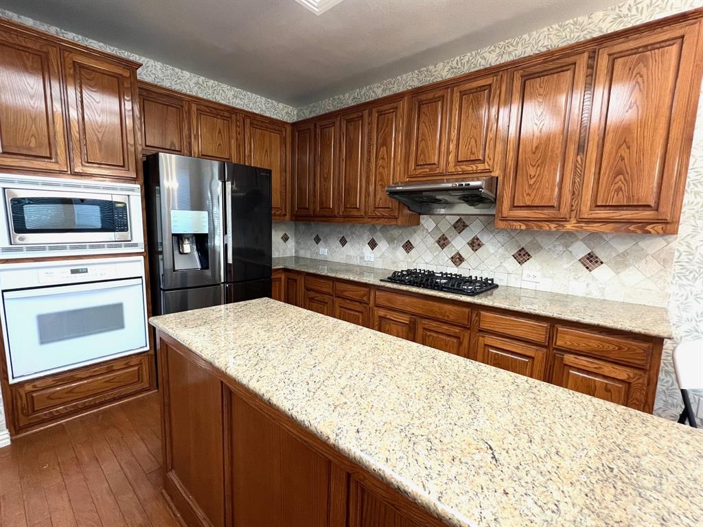 Kitchen featuring wood cabinetry, stone countertops, a center island, integrated stainless steel oven and microwave, and a gas cooktop