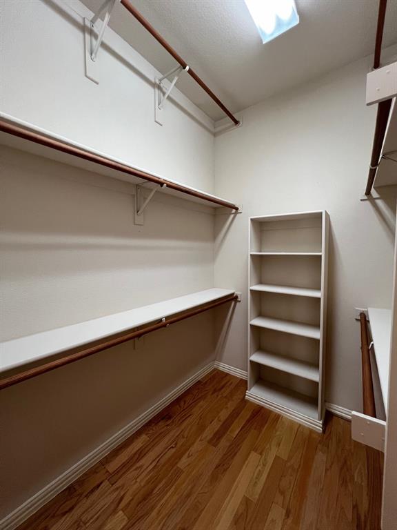 Walk-in closet featuring wood-finish flooring, integrated wall-to-wall shelving, multiple hanging rods, and a built-in vertical storage unit