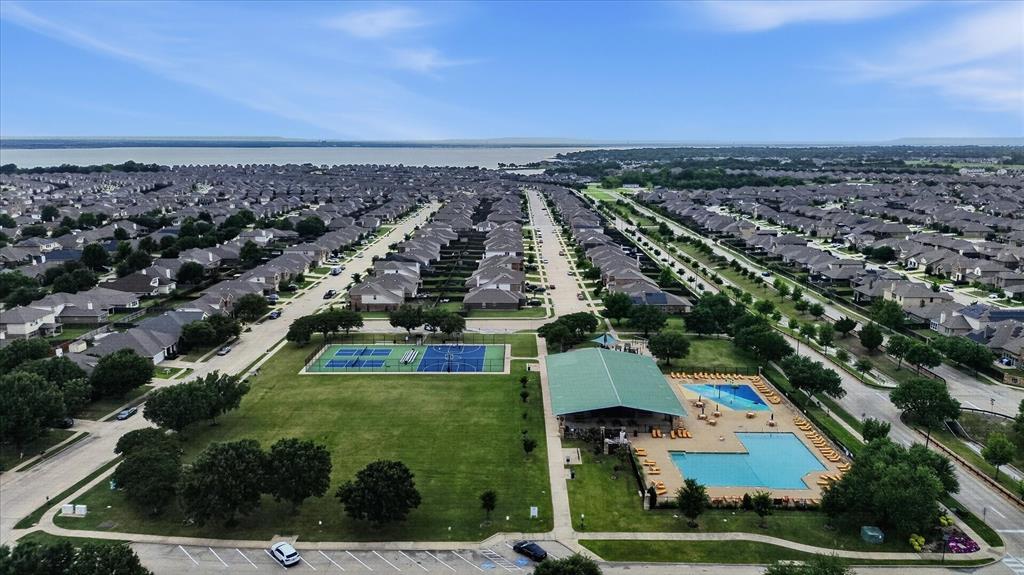 Aerial perspective of a community recreation area featuring swimming pools, a shaded pavilion, tennis courts, and expansive open green space