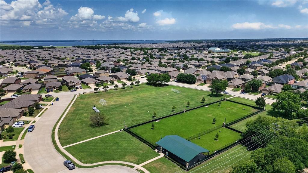 Aerial perspective of an expansive green space featuring a fenced-in lawn area, a metal-roof structure, and surrounding neighborhood infrastructure