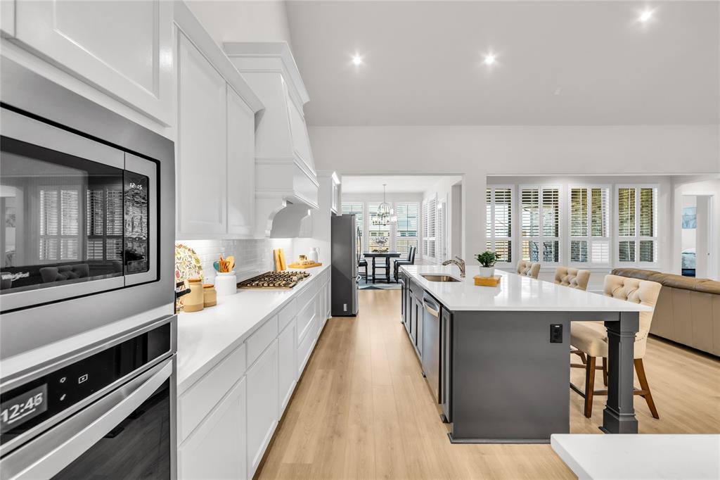 Kitchen featuring white shaker-style cabinetry, quartz countertops, a central island with a contrasting base, wood-finish flooring, and stainless-steel built-in appliances
