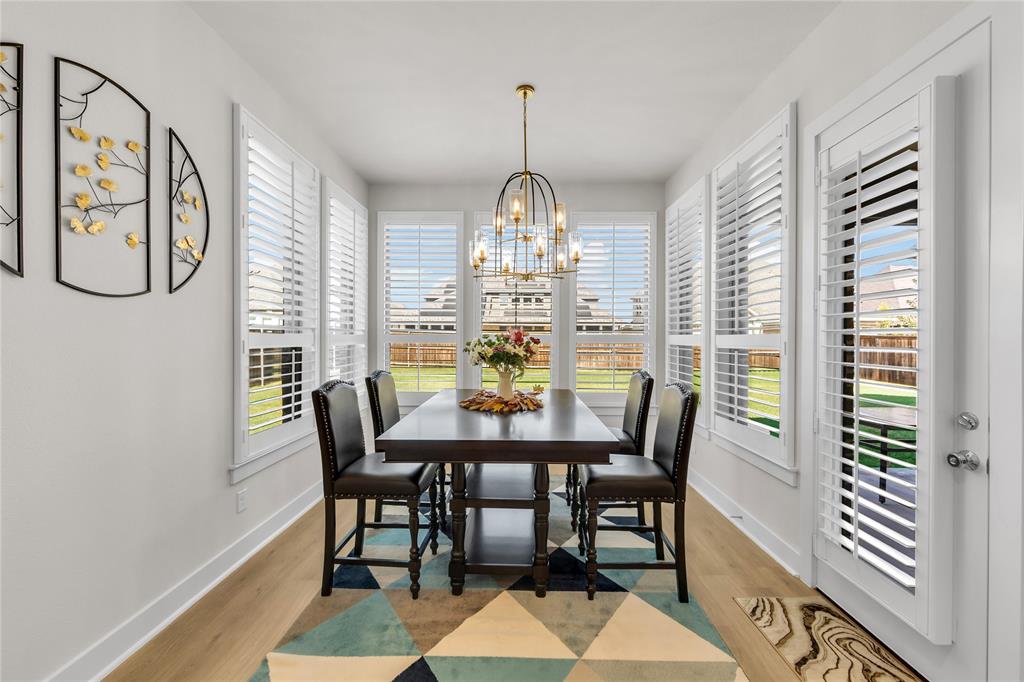 Dining area featuring wood-finish flooring, plantation shutters, a multi-light metal chandelier, and direct exterior access via a glass-paned door