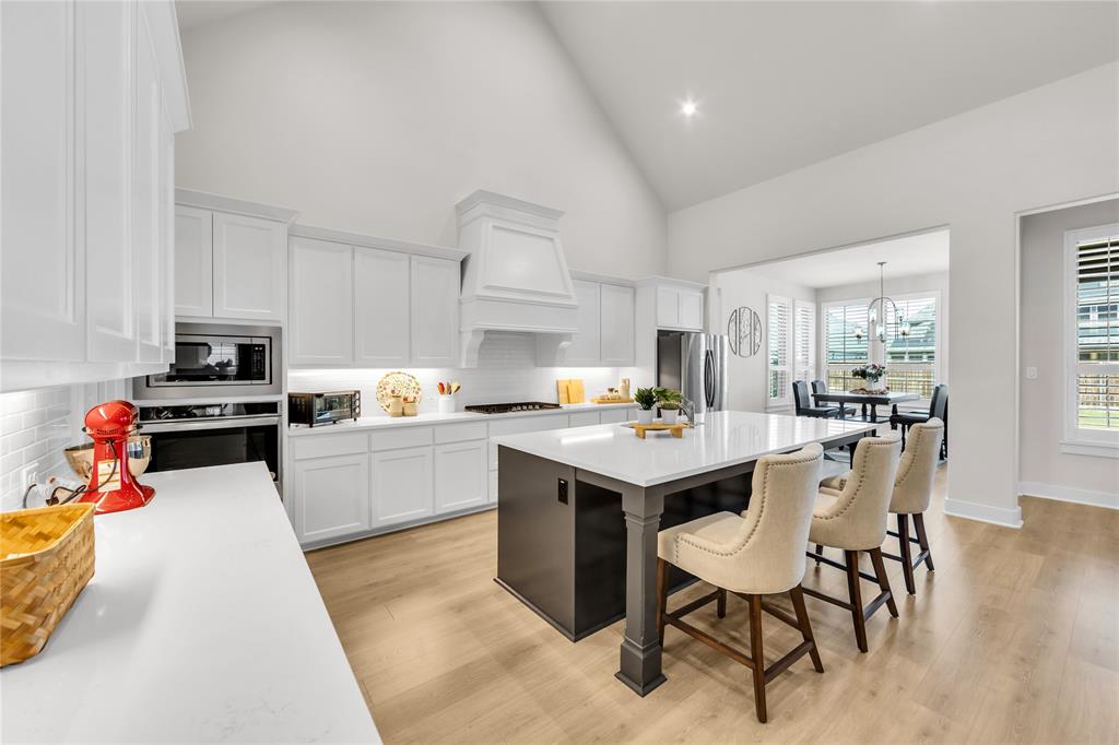 Kitchen featuring a vaulted ceiling, white cabinetry with integrated ventilation hood, central island with dark finish base, stone-surface countertops, and wood-finish flooring