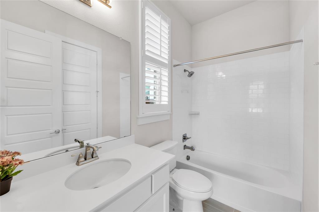 Bathroom featuring white vanity cabinetry, integrated sink, polished chrome faucet, white subway tile shower surround, and louvered shutters