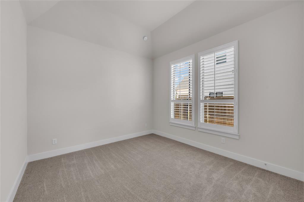 Neutral-toned room featuring a vaulted ceiling, wall-to-wall carpeting, and double windows fitted with white plantation shutters