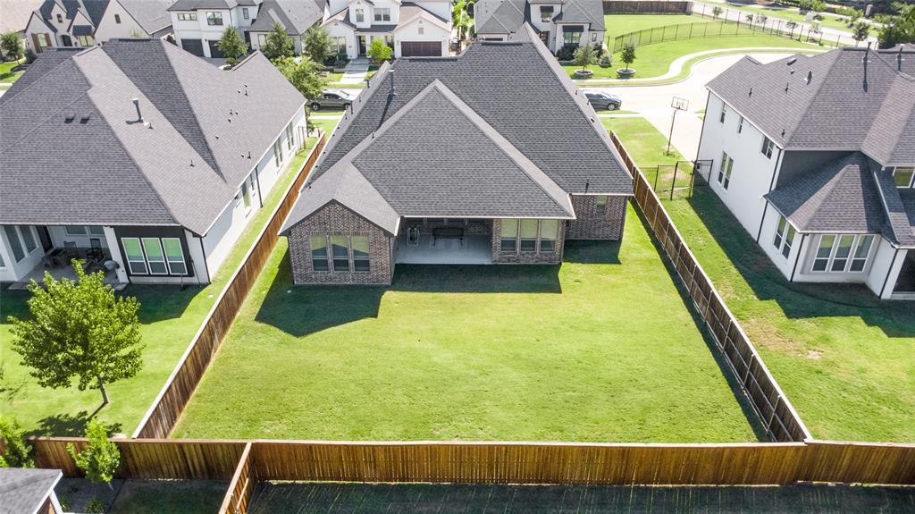 Aerial perspective of a multi-gabled brick residence featuring a covered patio and a fully enclosed wood-fenced rear yard with a grass lawn