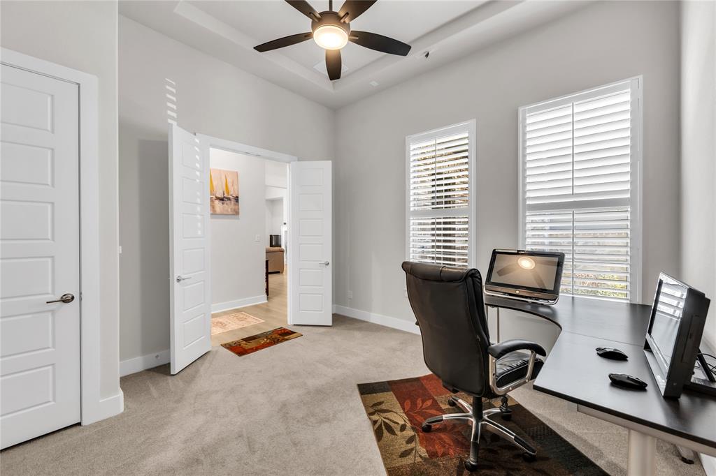 Room featuring high tray ceilings, a central ceiling fan, two windows with plantation shutters, and interior doors with a five-panel design