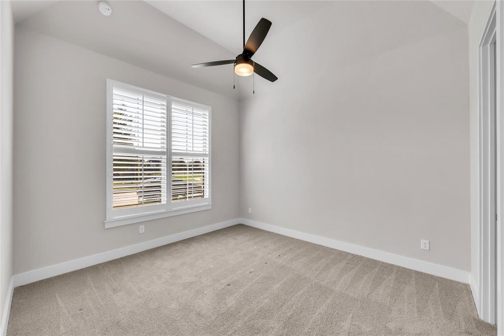 Vaulted ceiling featuring a central three-blade ceiling fan with integrated lighting, window with white plantation shutters, and neutral carpeting