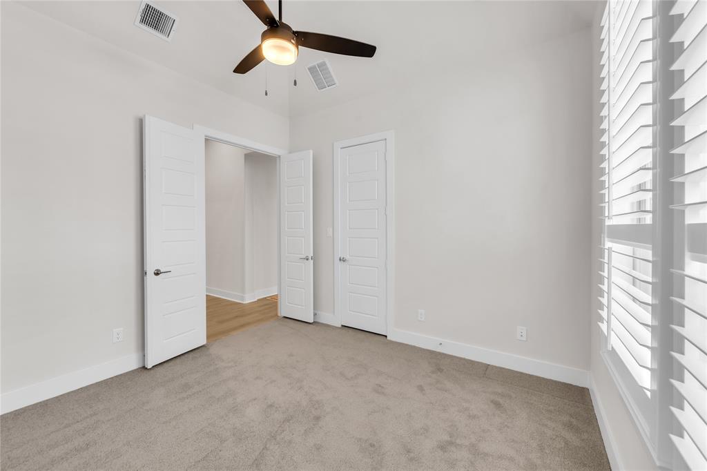 Room featuring neutral carpeted flooring, white interior doors, plantation shutters, and a ceiling fan with integrated lighting