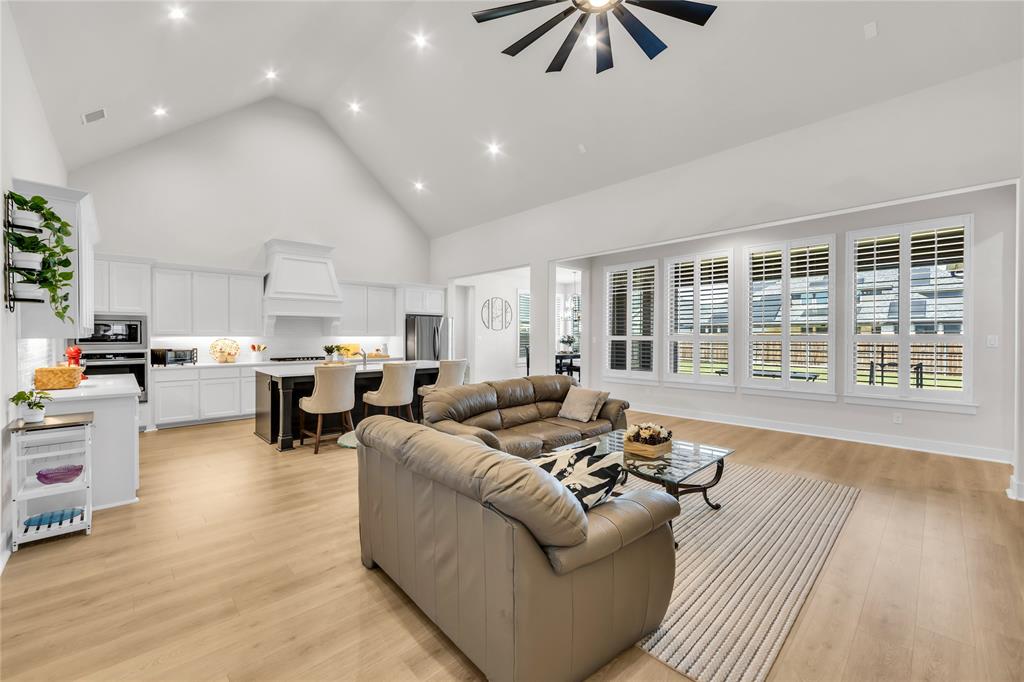 Open-concept kitchen and living area featuring vaulted ceilings, wood-finish flooring, recessed lighting, white cabinetry, and windows equipped with plantation shutters