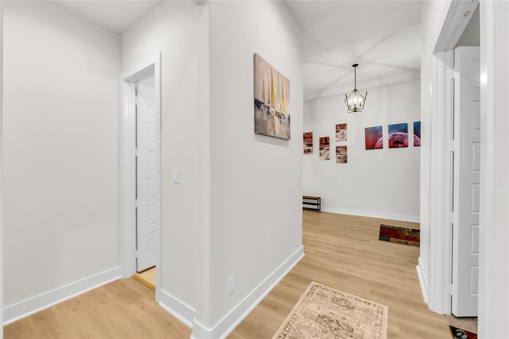Interior hallway featuring wood-finish flooring, white walls, multi-panel interior doors, and a decorative pendant light fixture
