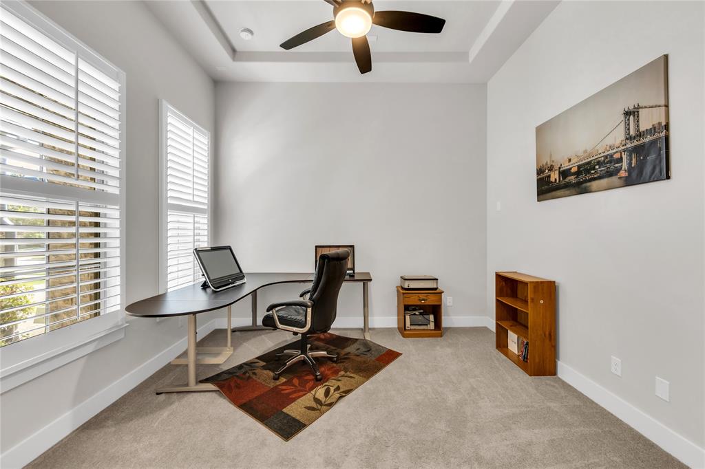 Room featuring neutral carpeting, tray ceiling with a multi-blade ceiling fan, and windows outfitted with plantation shutters